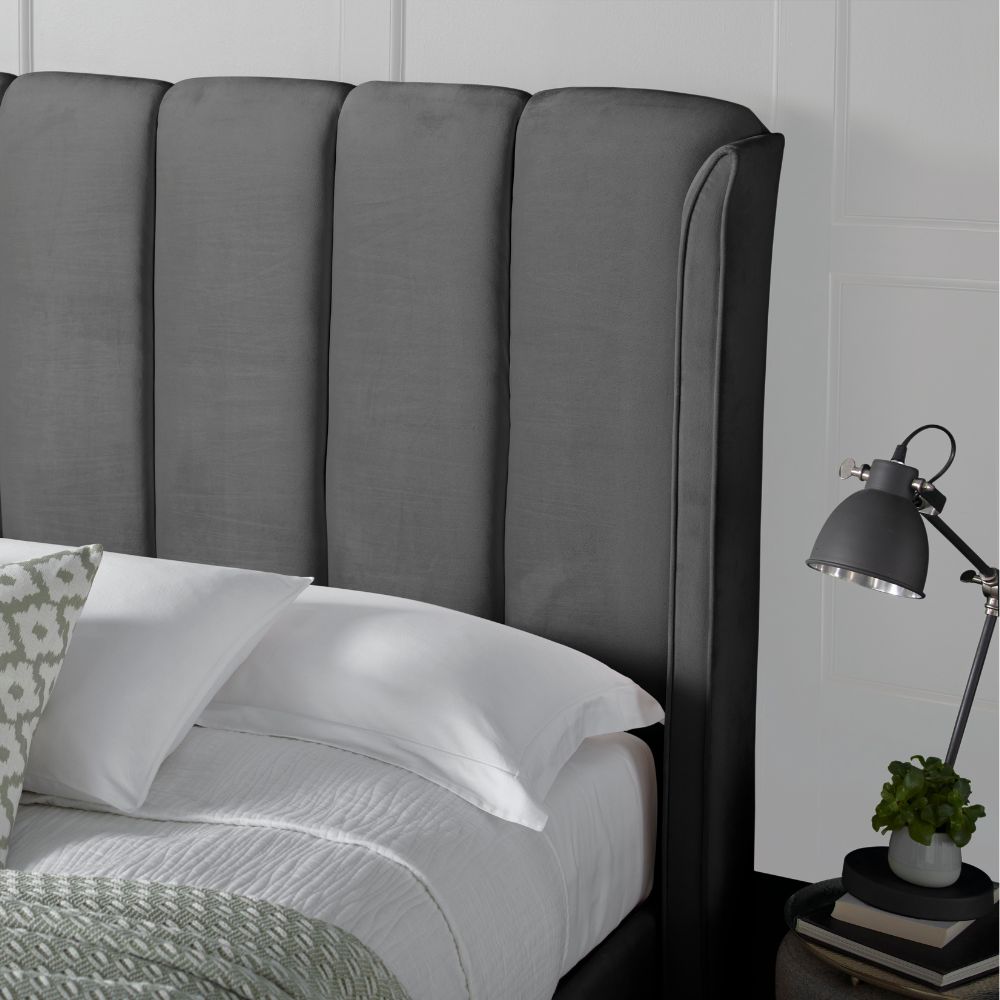 Grey upholstered headboard with a bed and lamp in a bedroom setting.