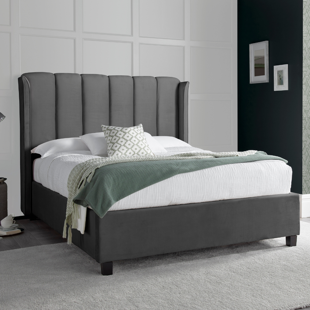 A Aurora Grey Velvet Ottoman bed frame with white bedding and a grey rug.
