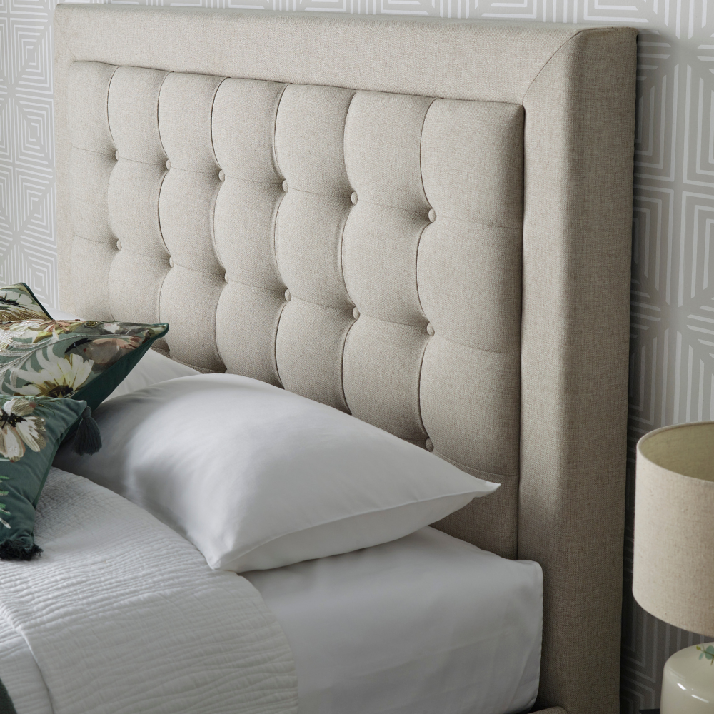 Beige upholstered headboard with pillows and a lamp in a bedroom setting