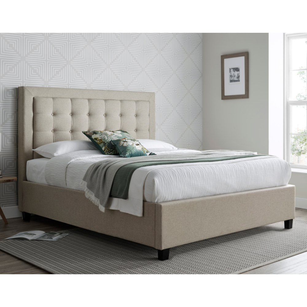 Beige upholstered bed in a room with patterned wallpaper and a window.