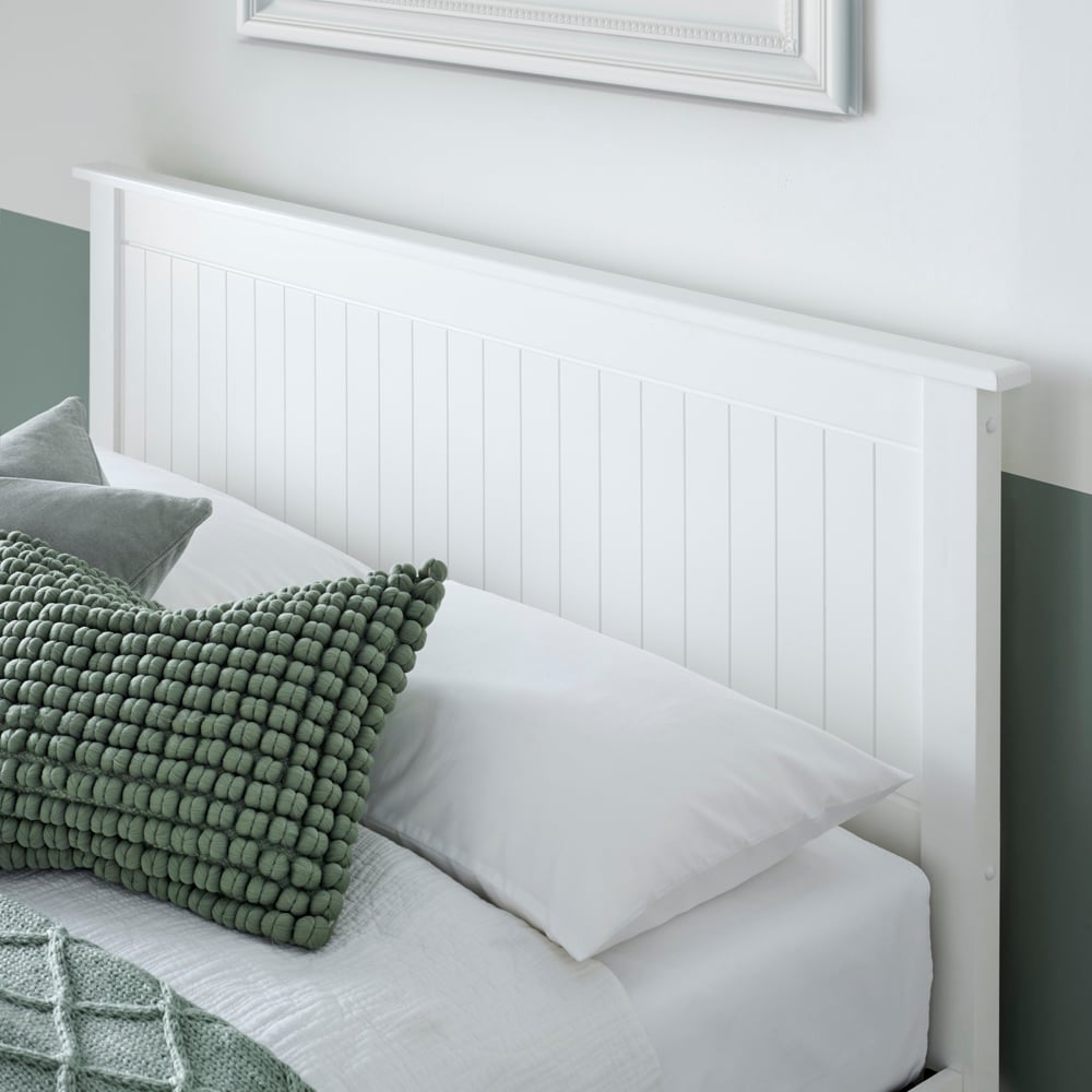 Bed with white headboard, green and grey pillows, and a framed picture on the wall.