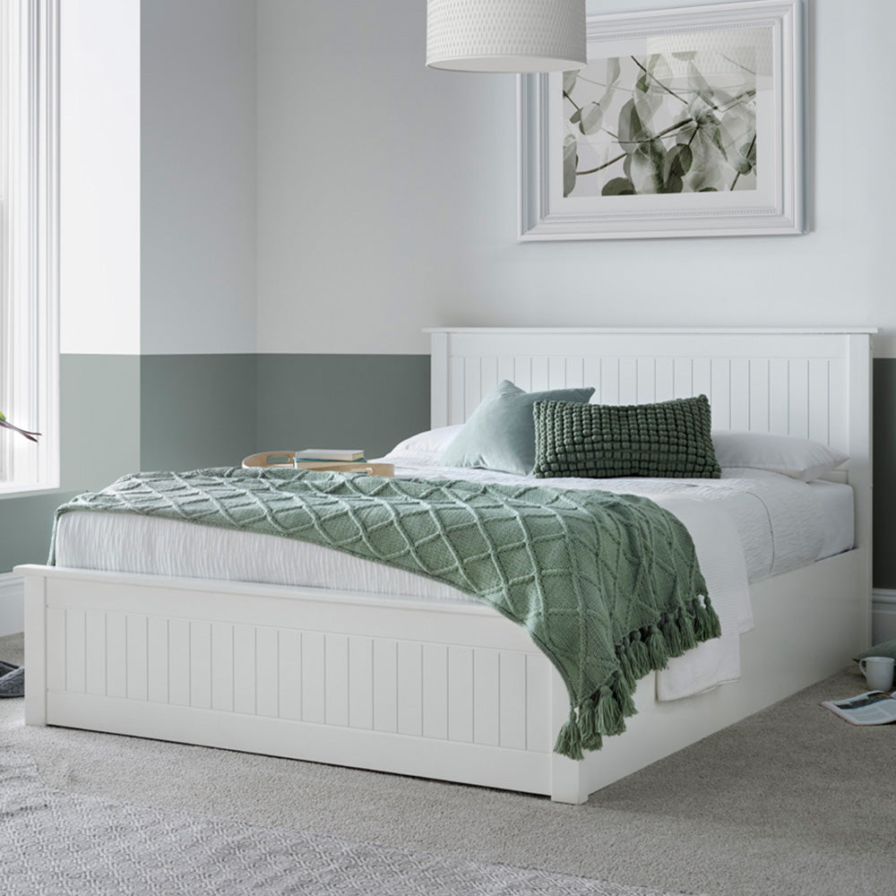 White bed with green blanket and pillows in a bedroom setting