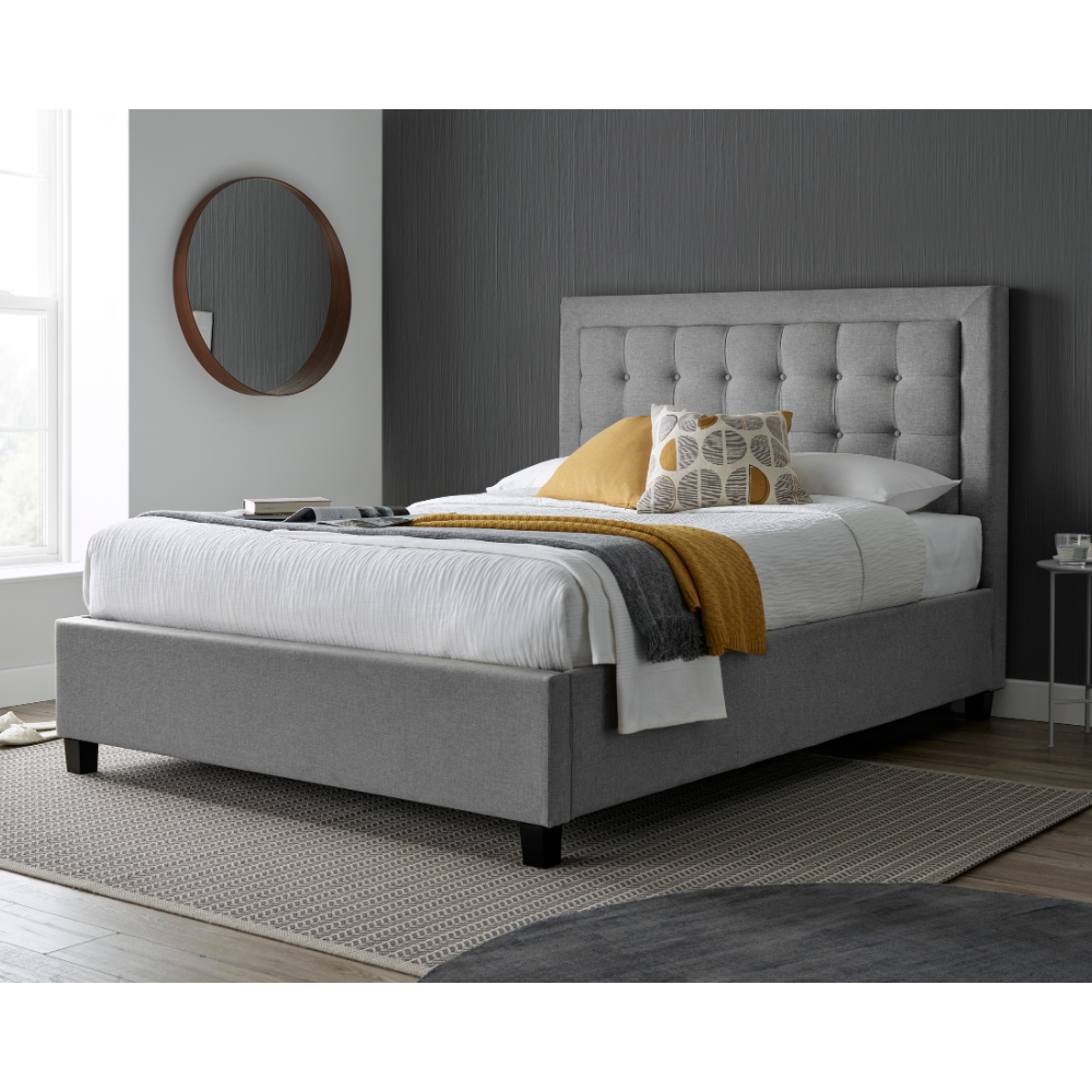 Grey upholstered bed with white bedding and yellow blanket in a bedroom setting.