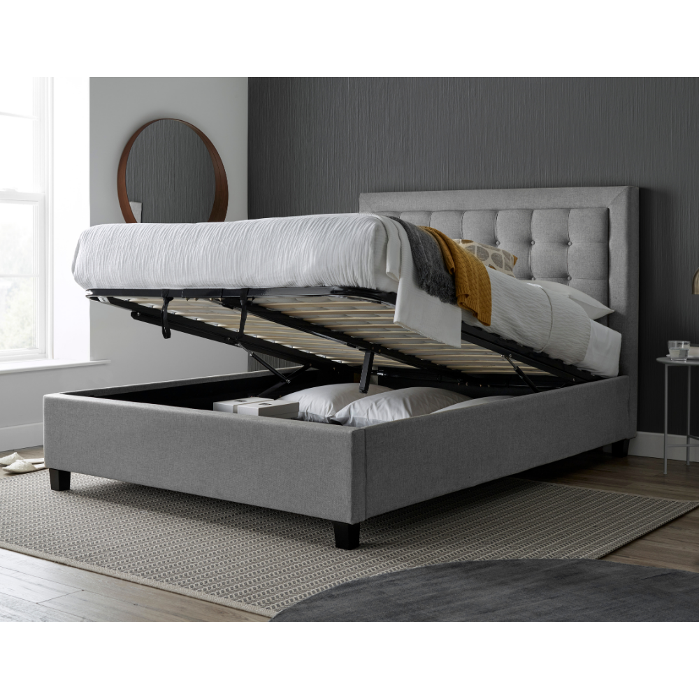 Grey upholstered bed with storage drawers in a room with a mirror and small table.