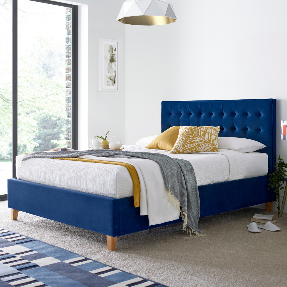 Blue upholstered bed with white bedding and yellow pillows in a modern bedroom.