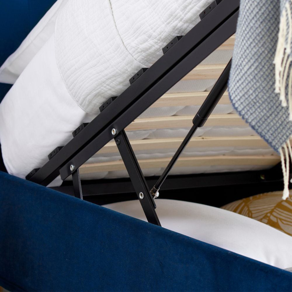 Close-up of a ottoman bed frame with a white blanket and blue towel on a wooden surface.