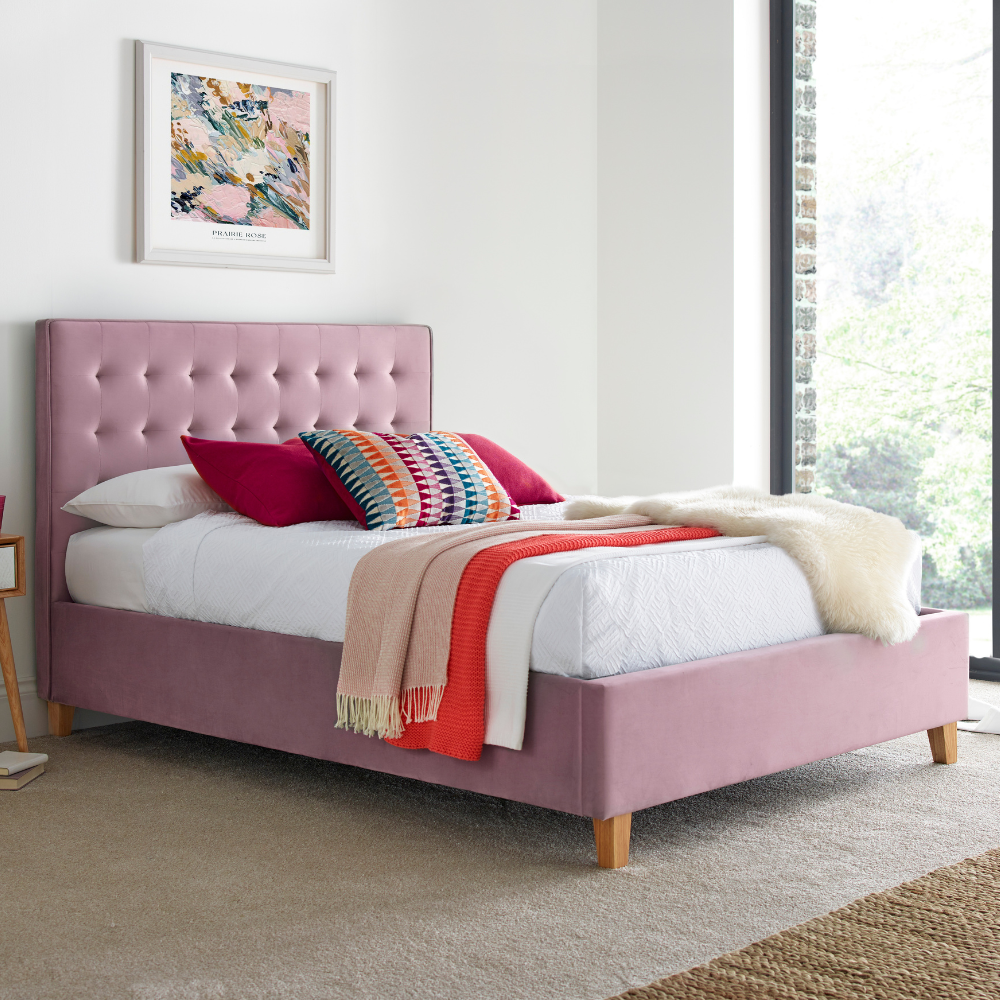 Pink upholstered bed in a room with a painting on the wall.