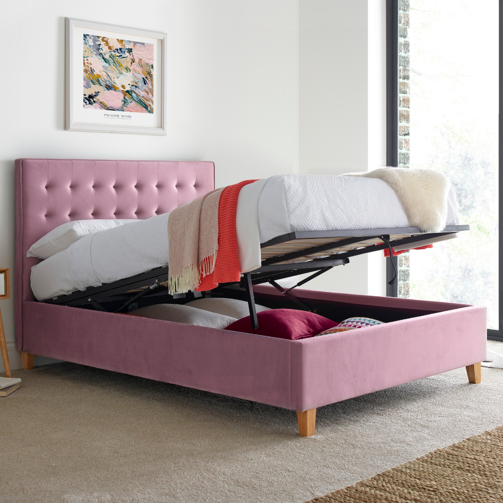 Pink upholstered bed with mattress lifted in a room with a painting on the wall.