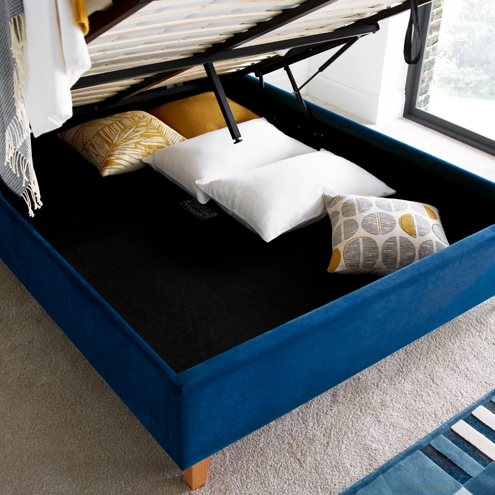 Blue ottoman bed with mattress lifted up and pillows in the underbed storage.