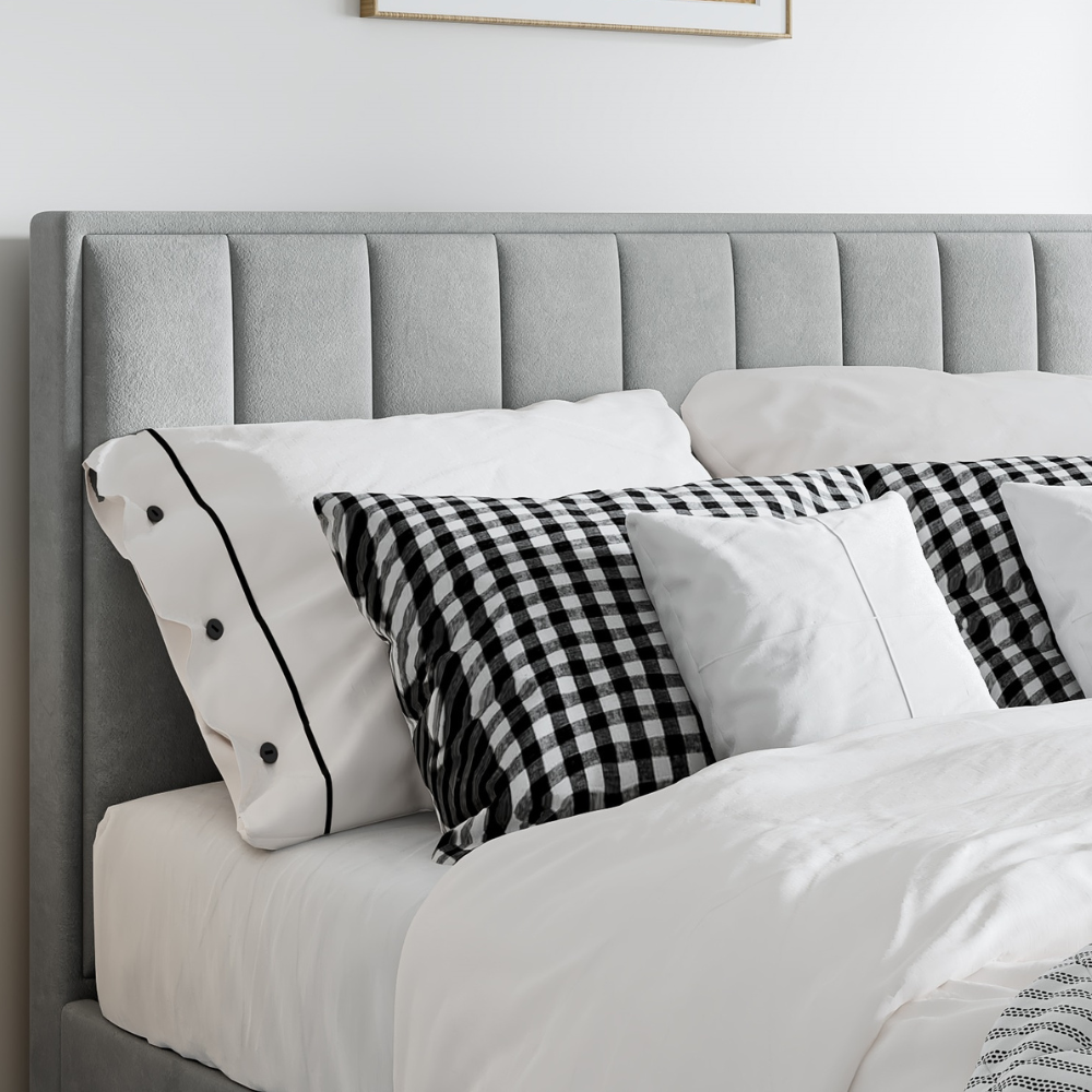 Grey upholstered headboard with white and plaid pillows on a bed.