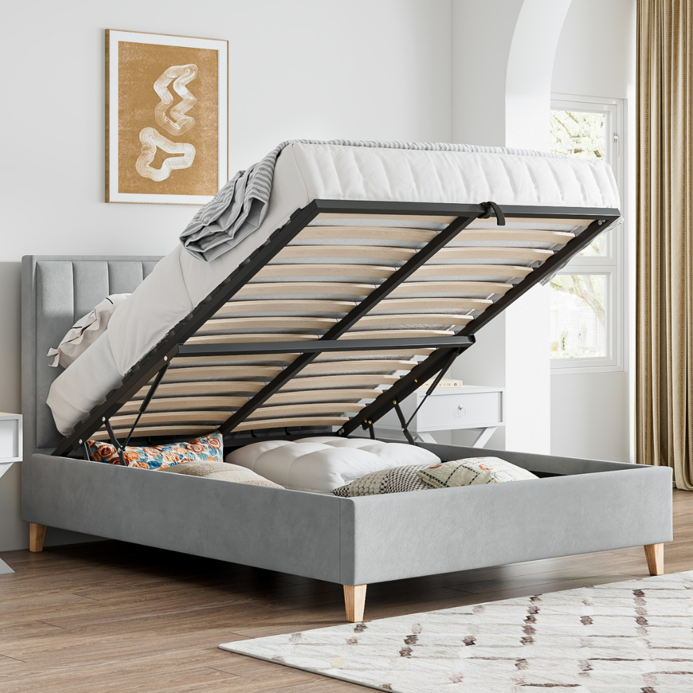 Grey upholstered bed with wooden slats in a room with a window and artwork on the wall.