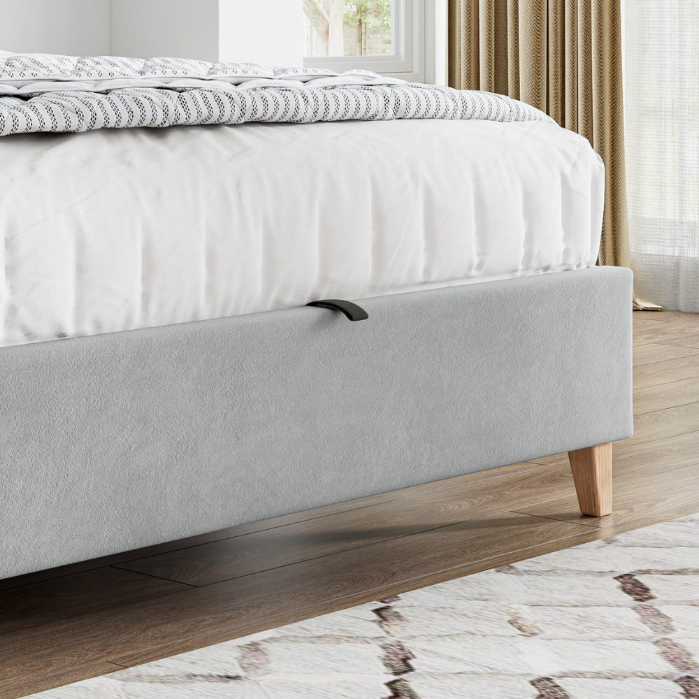 Grey upholstered bed with wooden legs in a bedroom setting.
