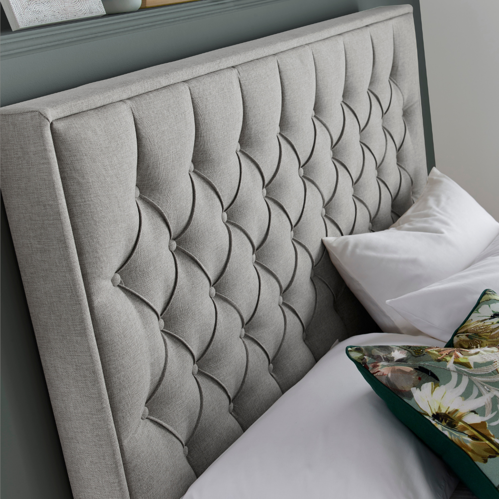 Grey tufted headboard with decorative pillows on a bed