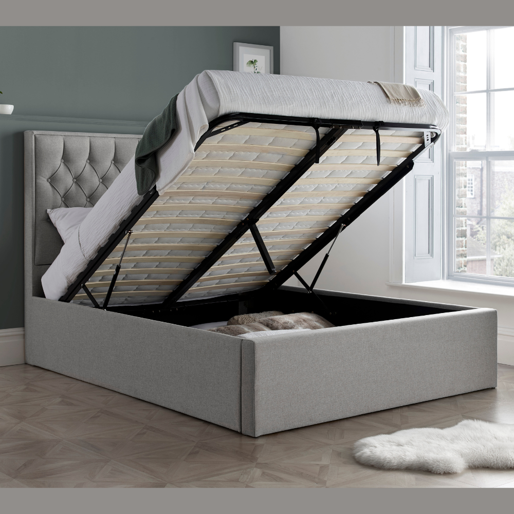 Grey upholstered bed with open storage compartment in a room with a window.