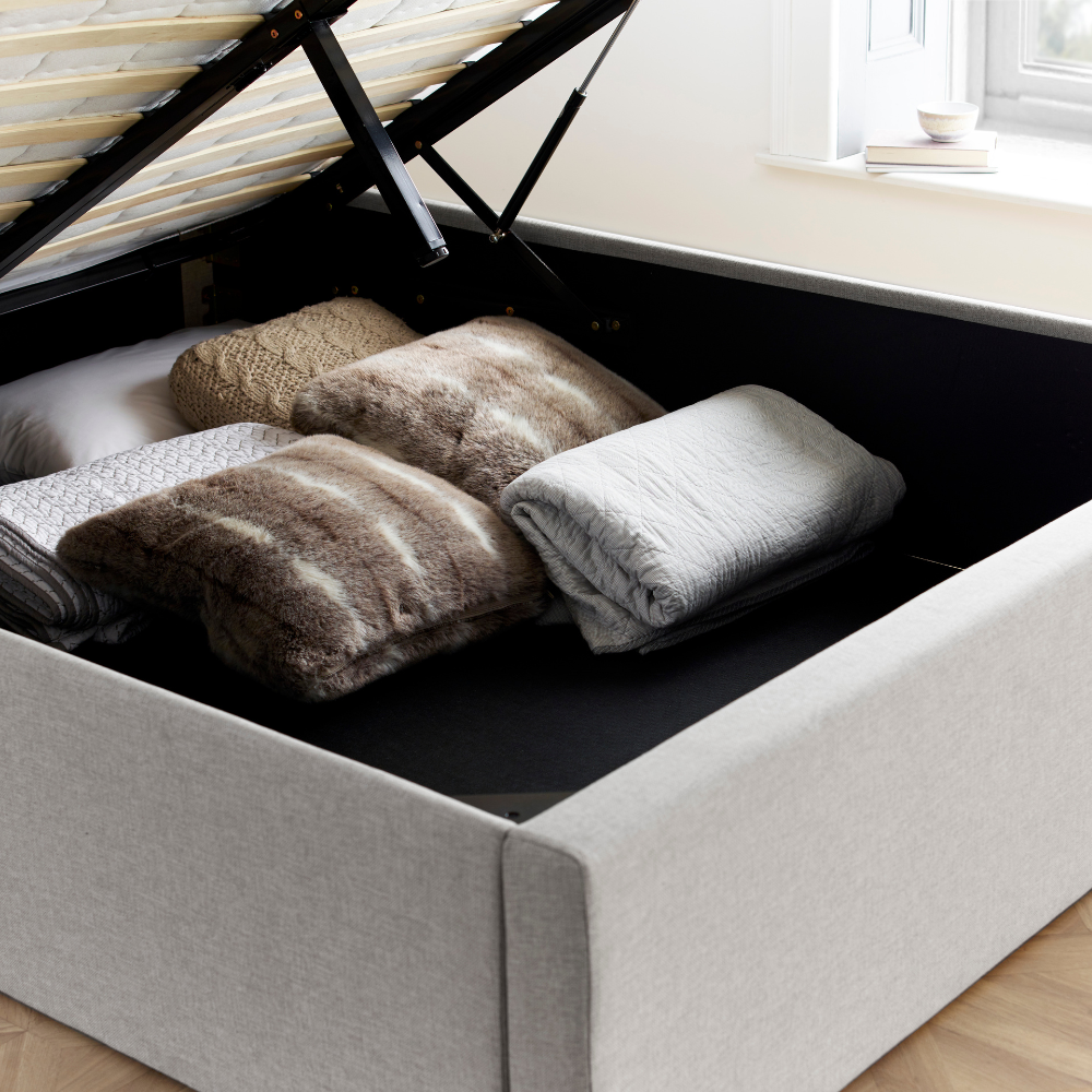 Bed with storage compartment containing folded towels and pillows.