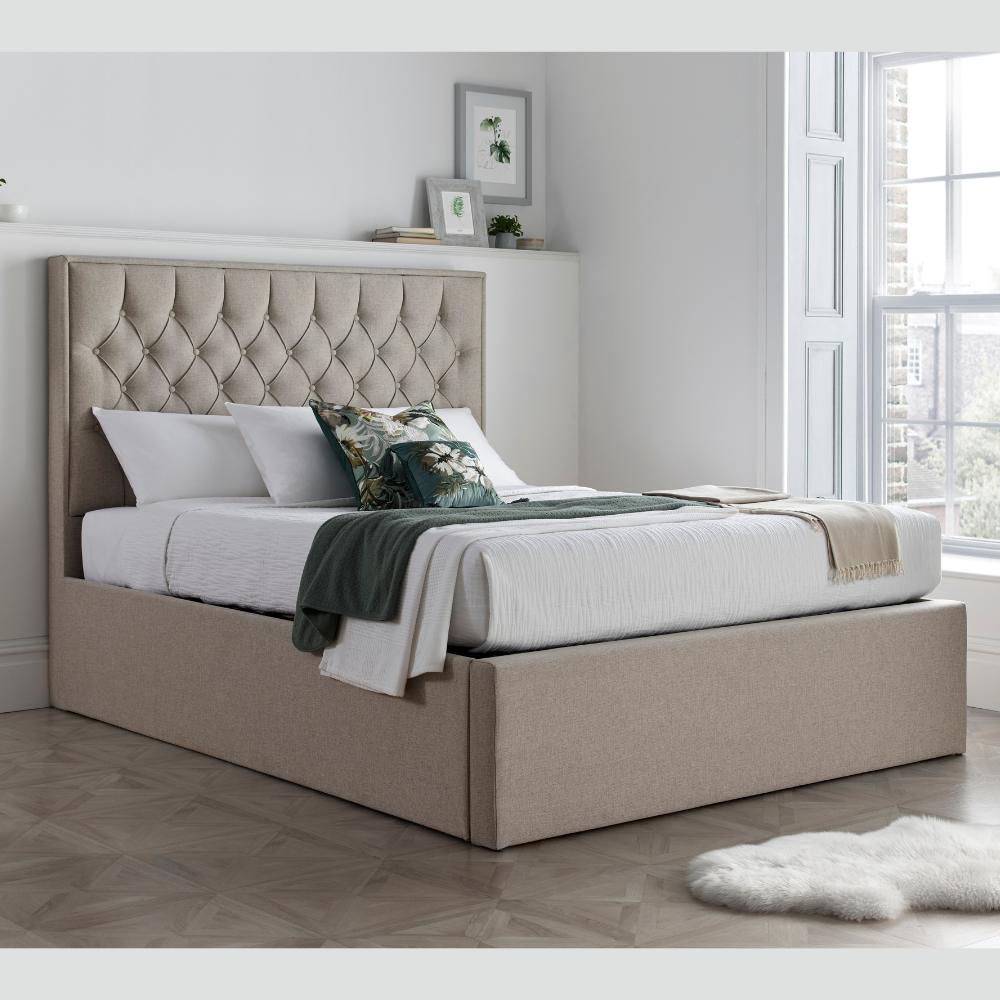 Beige upholstered bed with tufted headboard in a room with a window and framed pictures.