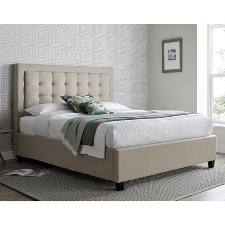 Beige upholstered bed in a room with patterned wallpaper and a window.