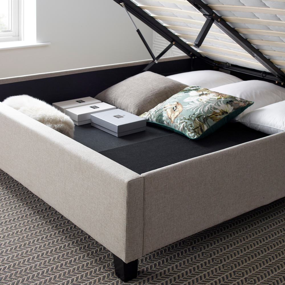 Beige upholstered bed with storage compartment and decorative pillows in a room.