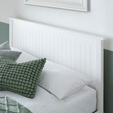 Bed with white headboard, green and grey pillows, and a framed picture on the wall.
