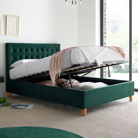 Green upholstered ottoman bed frame opened in a white bedroom. 
