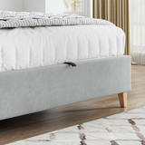 Grey upholstered bed with wooden legs in a bedroom setting.