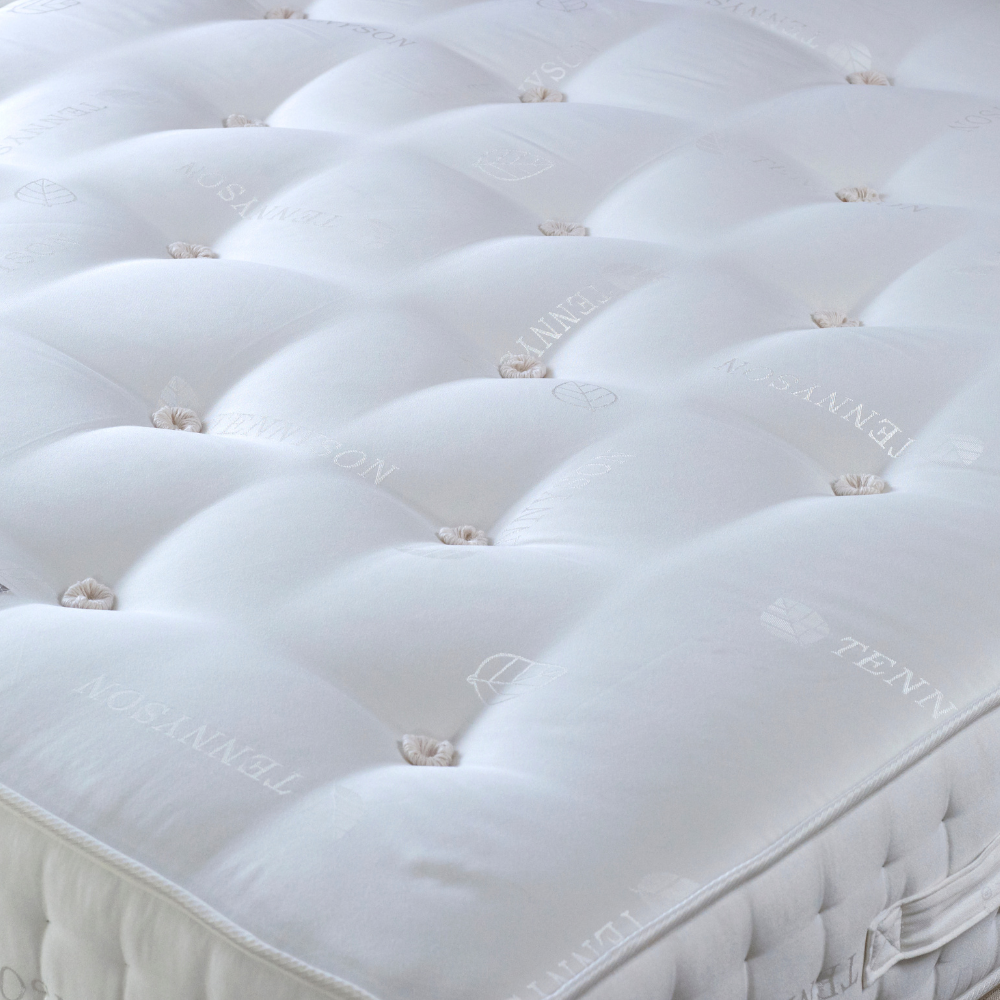 Close-up of a white mattress with tufted design and brand name.